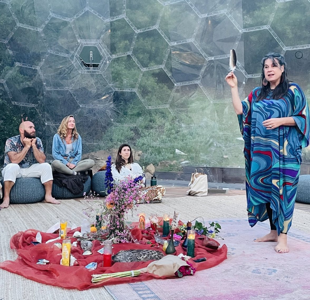 Leah leading a ceremony, feather raised, altar of flowers at her feet