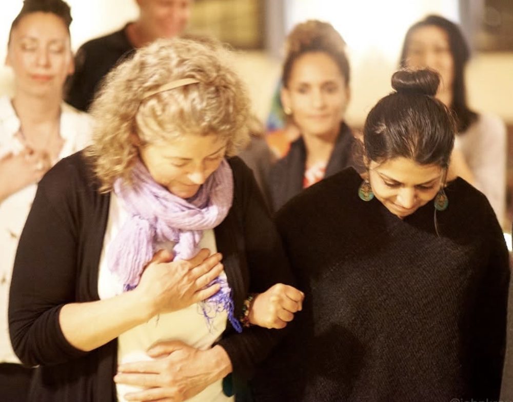 Two women embracing during a ceremony, hand on heart